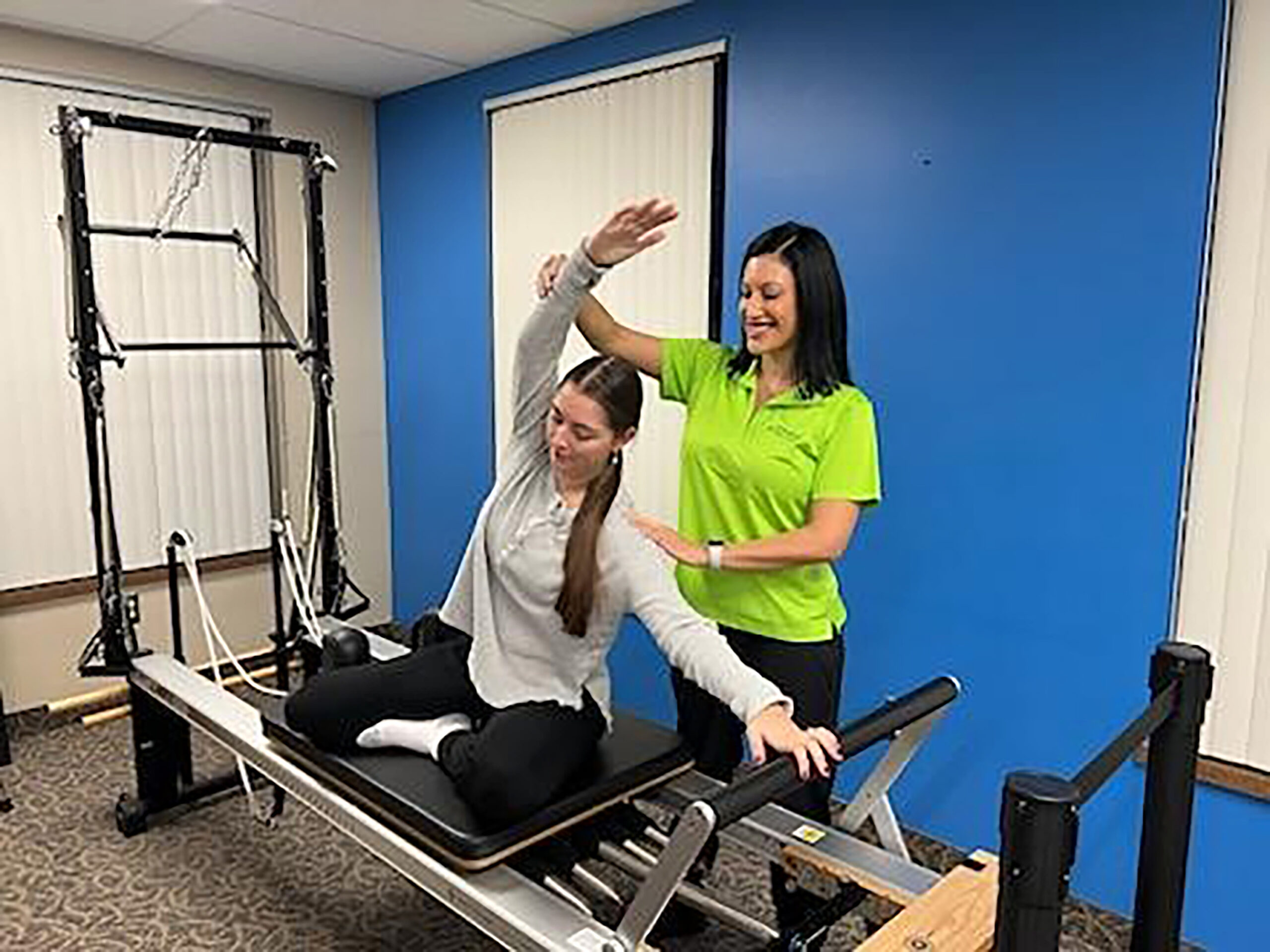 Picture of Dr. Orille assisting a young woman with trunk and shoulder flexion on a Pilates reformer.