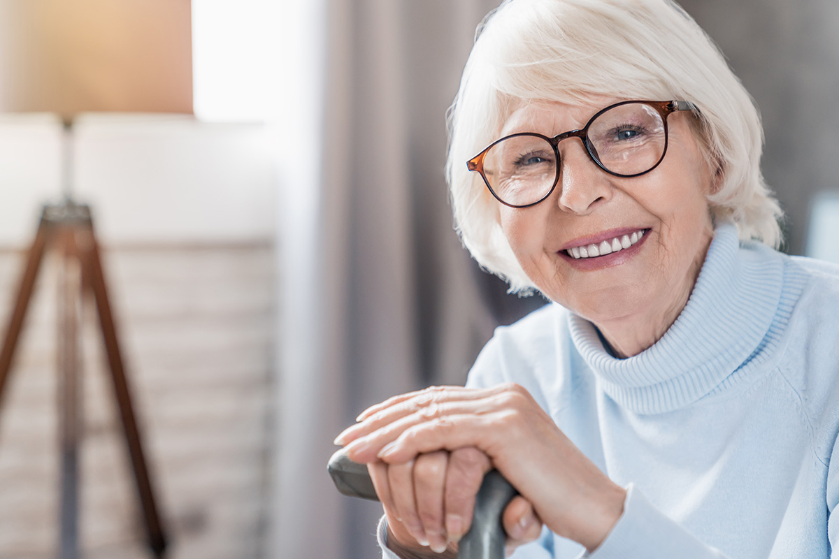 Portrait of happy mature woman in eyeglasses holding cane while sitting on sofa at home. cane and smiling.